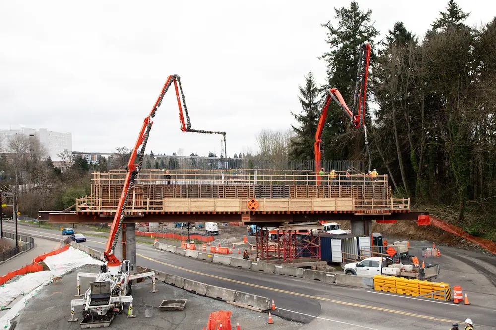 Two Alliance concrete pump trucks place pier caps for the future 1,587‑foot‑long SR 509 Expressway bridge in SeaTac.