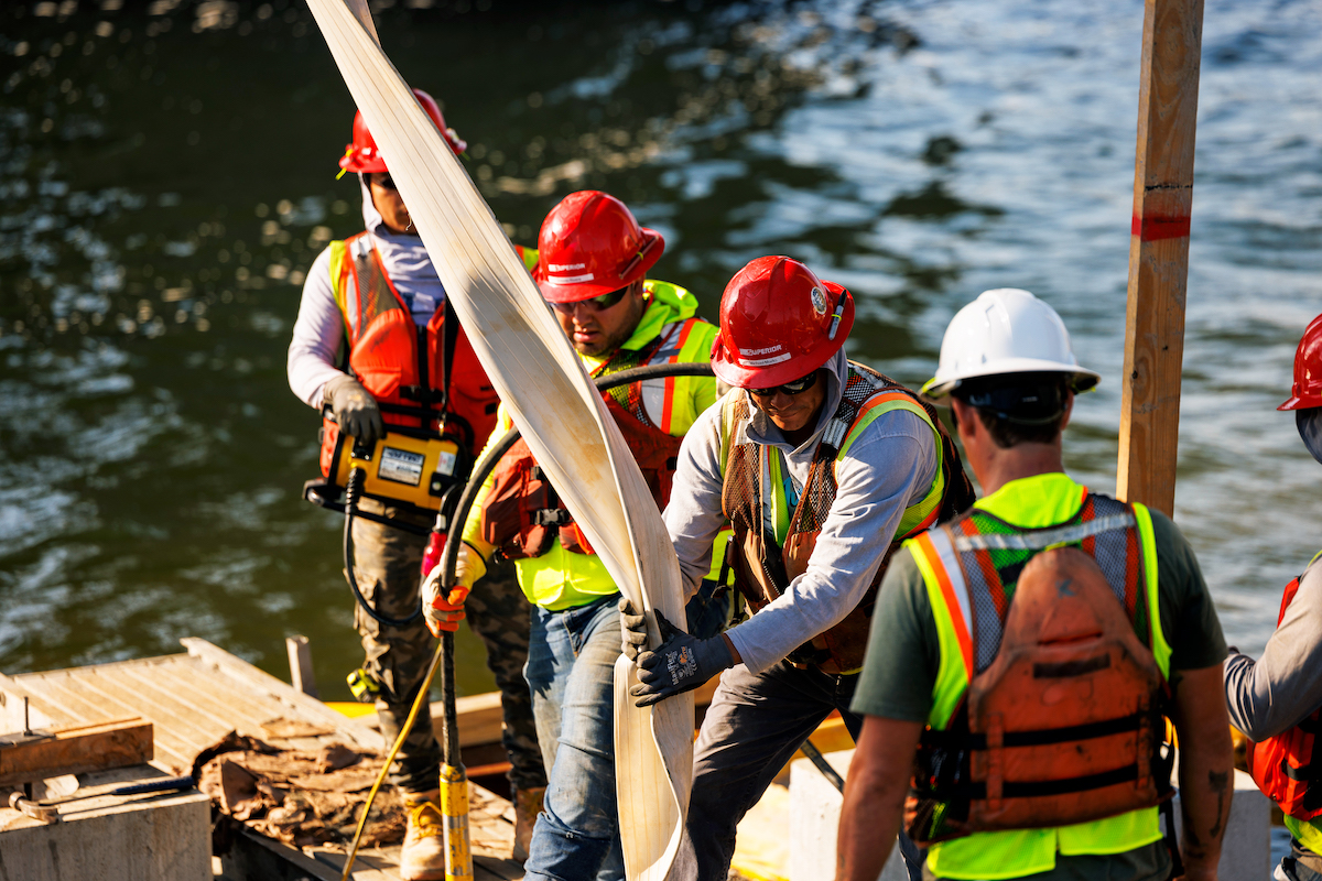 Concrete is placed for the new Brooks Bridge pier structure through a crane-delivered concrete bucket system.