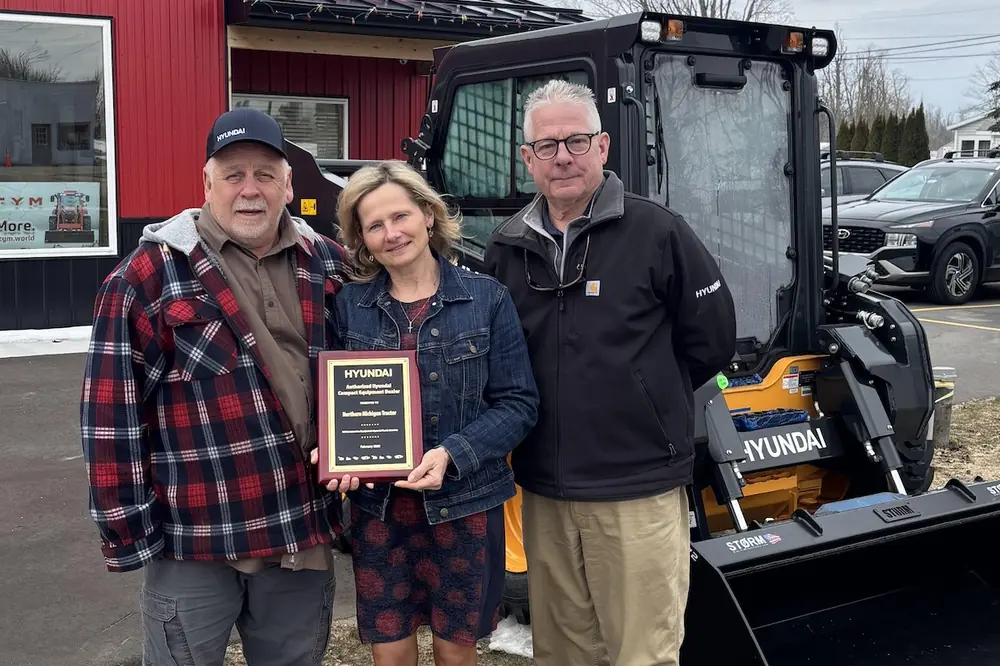 Joe and Eva Grusczynski, Owners of Northern Michigan Tractor, display their Hyundai dealer plaque presented to them by Rich Desmond (right), District Sales Manager, HD Hyundai Construction Equipment North Americas.