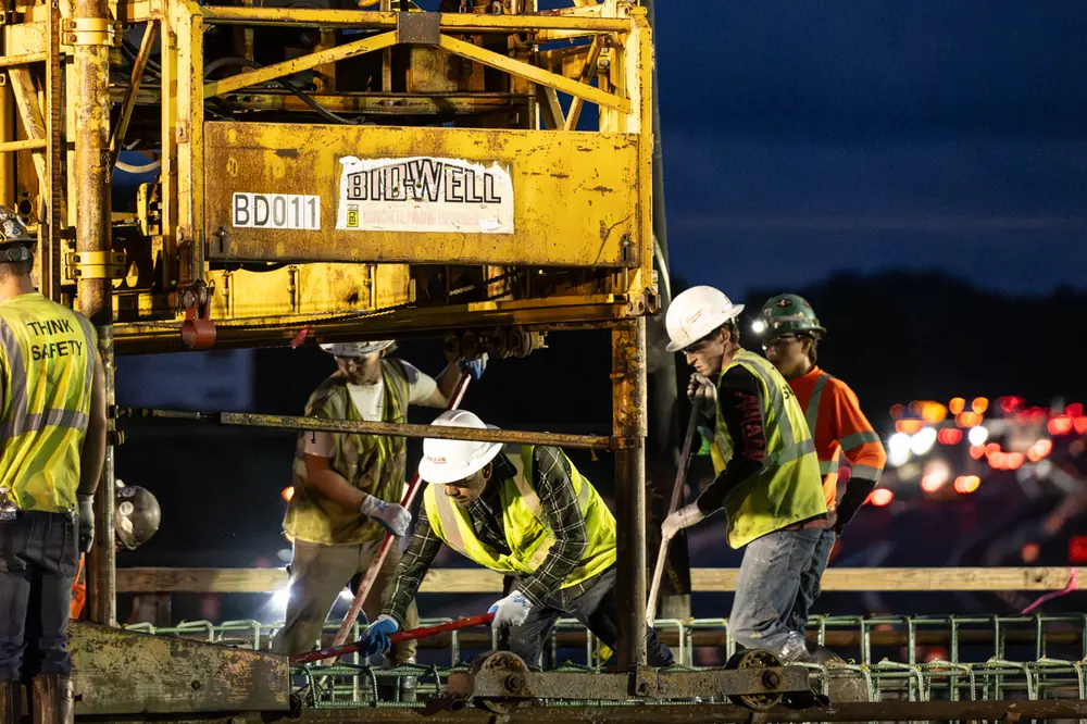 Workers on the Marshall Modernization Project use a Bid-Well concrete paving machine to place concrete on a bridge deck.