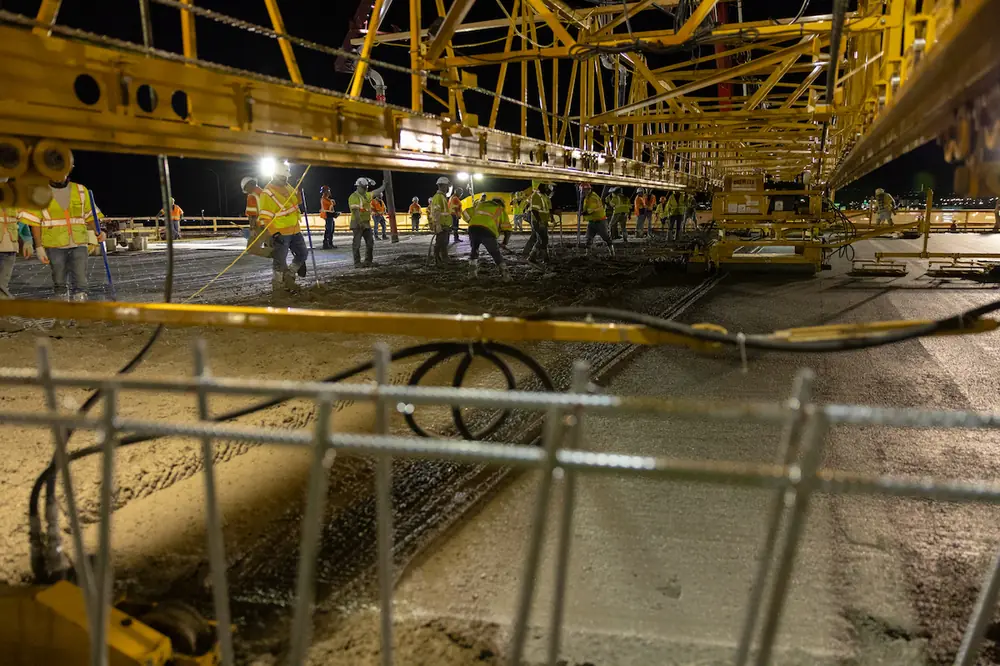 This photo is taken from under the concrete leveling machine as it moves along the new Montgomery deck over I-25. Crews work to level concrete that is brought up by two concrete pump trucks.