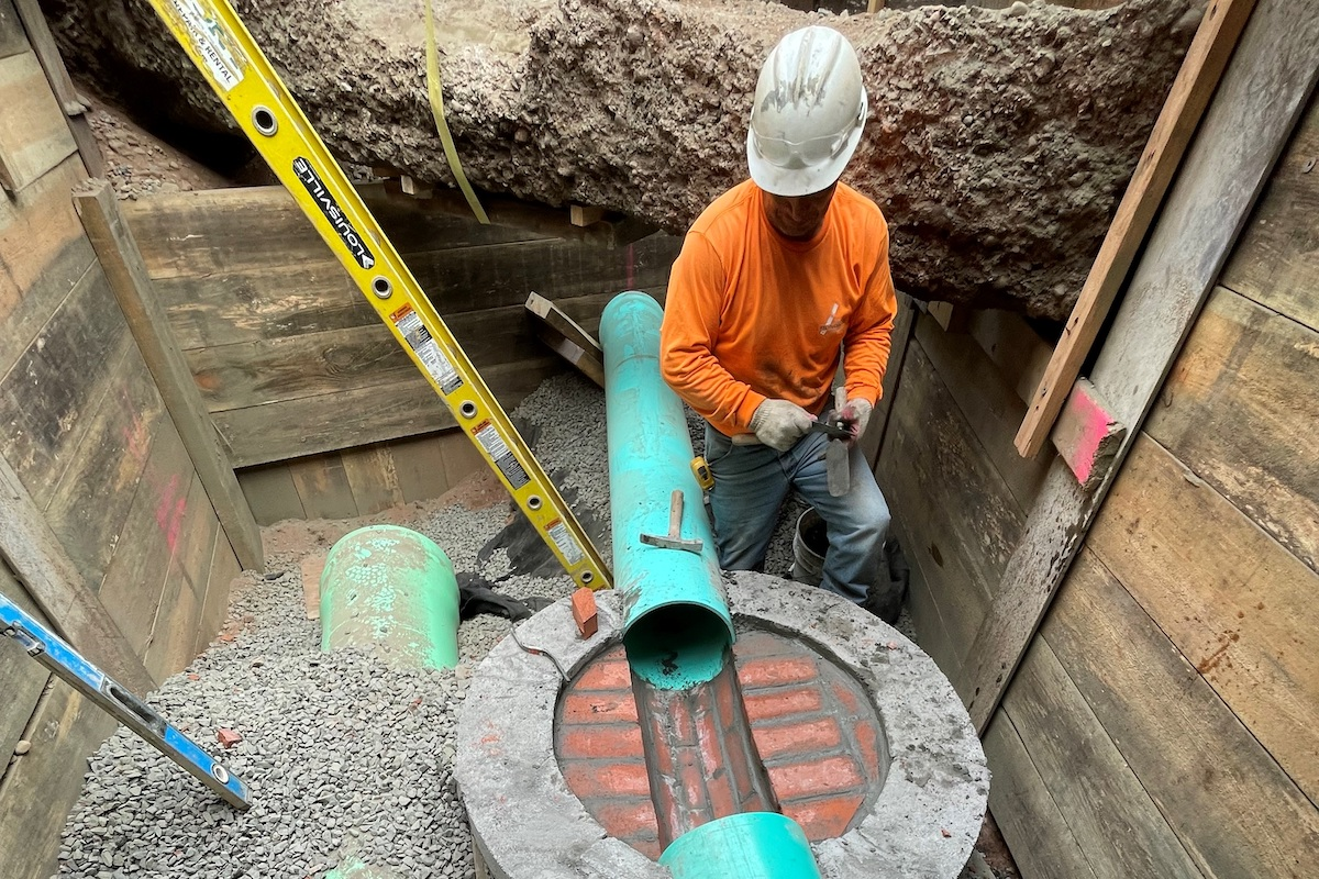 In a busy intersection in front of the Yale campus, a crewmember installs PVC sanitary sewer pipe in a common trench with PVC storm drain.