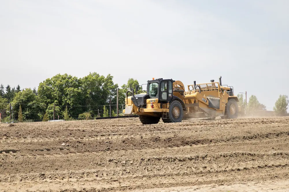 A crew member uses a Caterpillar 627K Scraper to move and haul earthwork, shaping and stabilizing the soil.