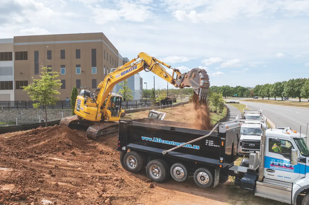 An operator deposits material into the bed of a truck with a Komatsu PC238USLC Excavator.