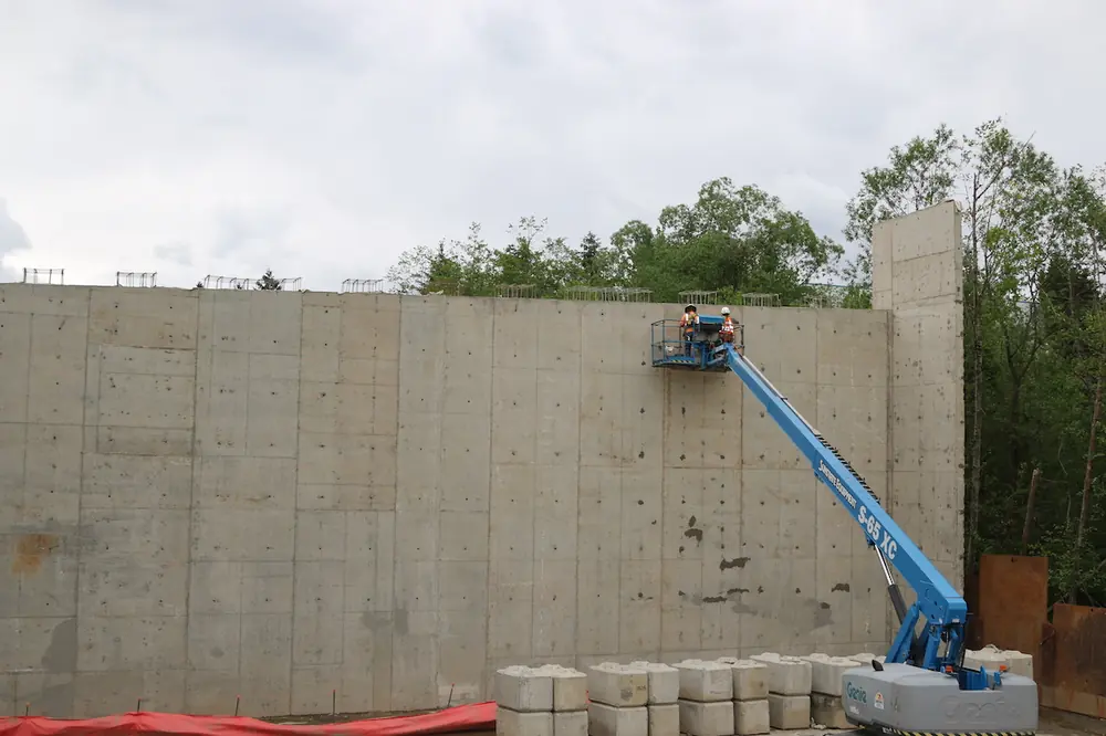 Two crew members work on finishing a bridge abutment wall with a Genie telescopic boom lift.