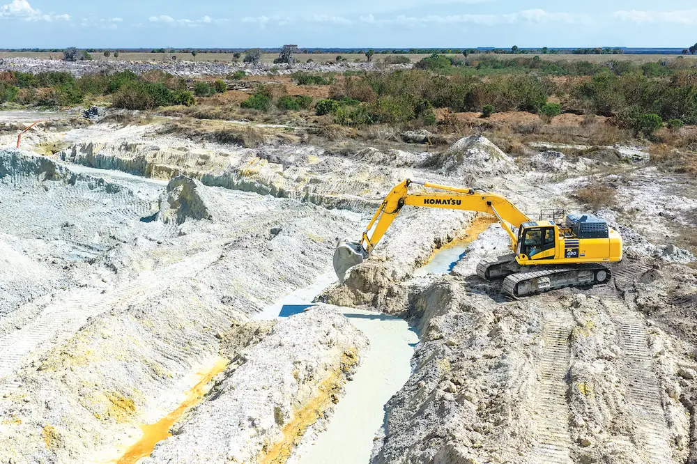To manage water while excavating a lake, an operator uses a Komatsu PC490LC Excavator to cut through a berm into precut trenches.