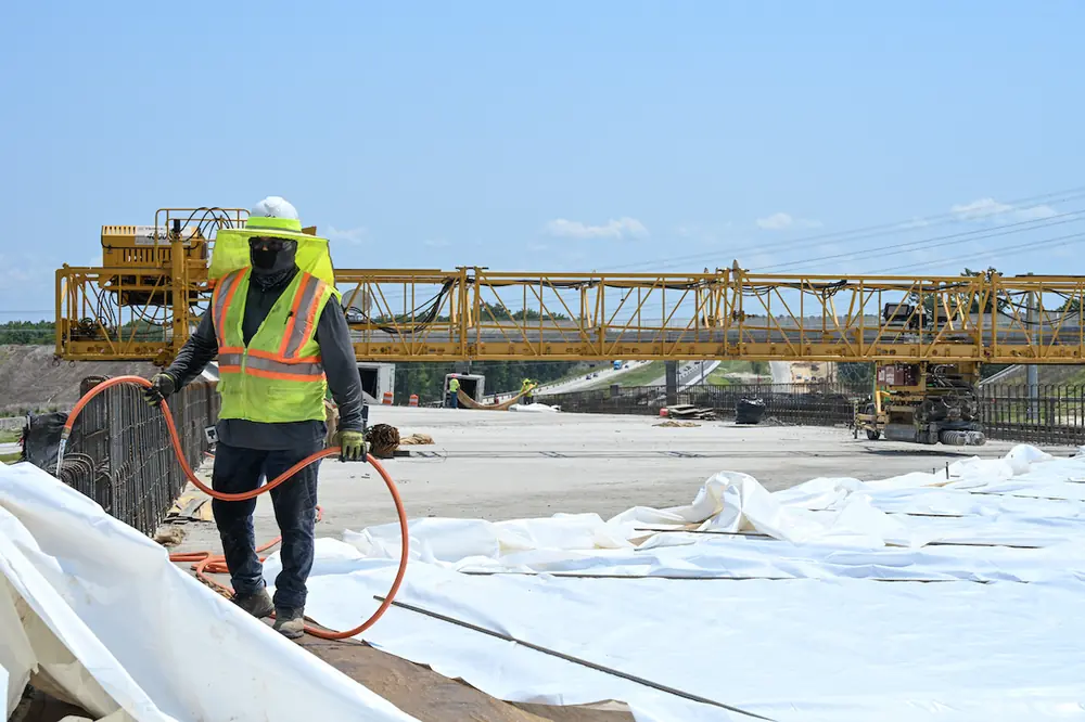 A contractor is wet curing a freshly poured concrete bridge deck near the project site.