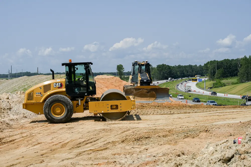 A roller and bulldozer compact and move material around the location of the new I-77 Exit 26 intersection overpass.