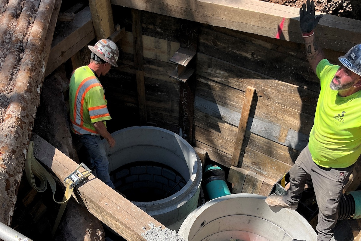 Crews install sewer and storm drain between a cluster of underground utilities in front of the Yale School of Management.